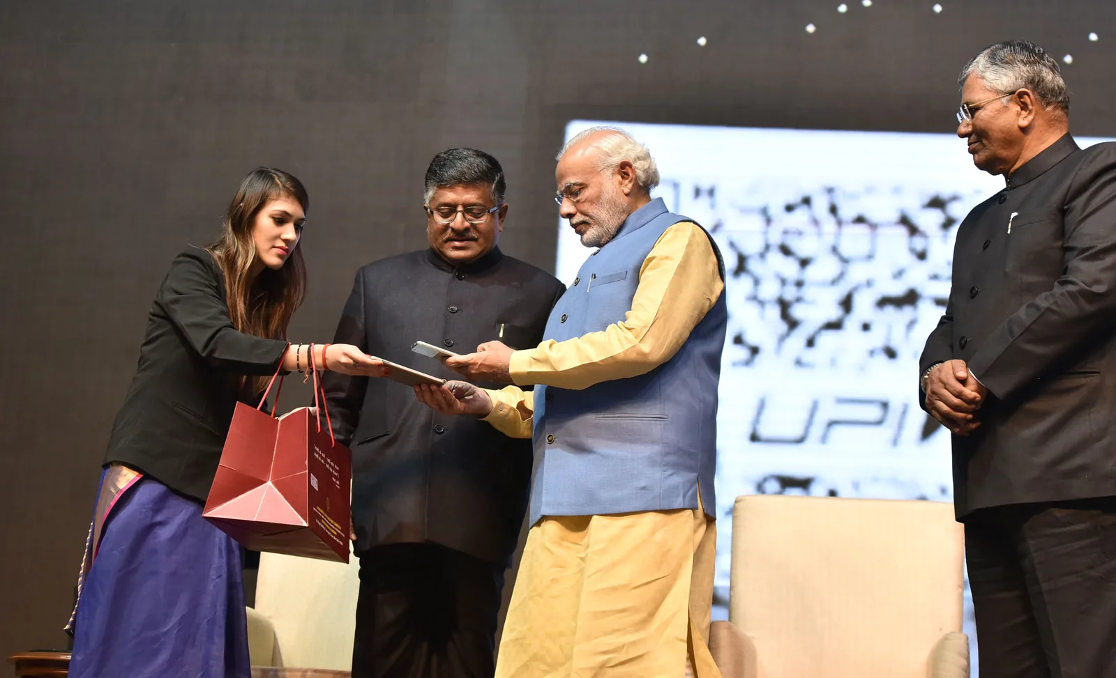 Narendra Modi on stage at DigiDhan Mela in New Delhi launching the BHIM mobile payments app, with a large screen behind him