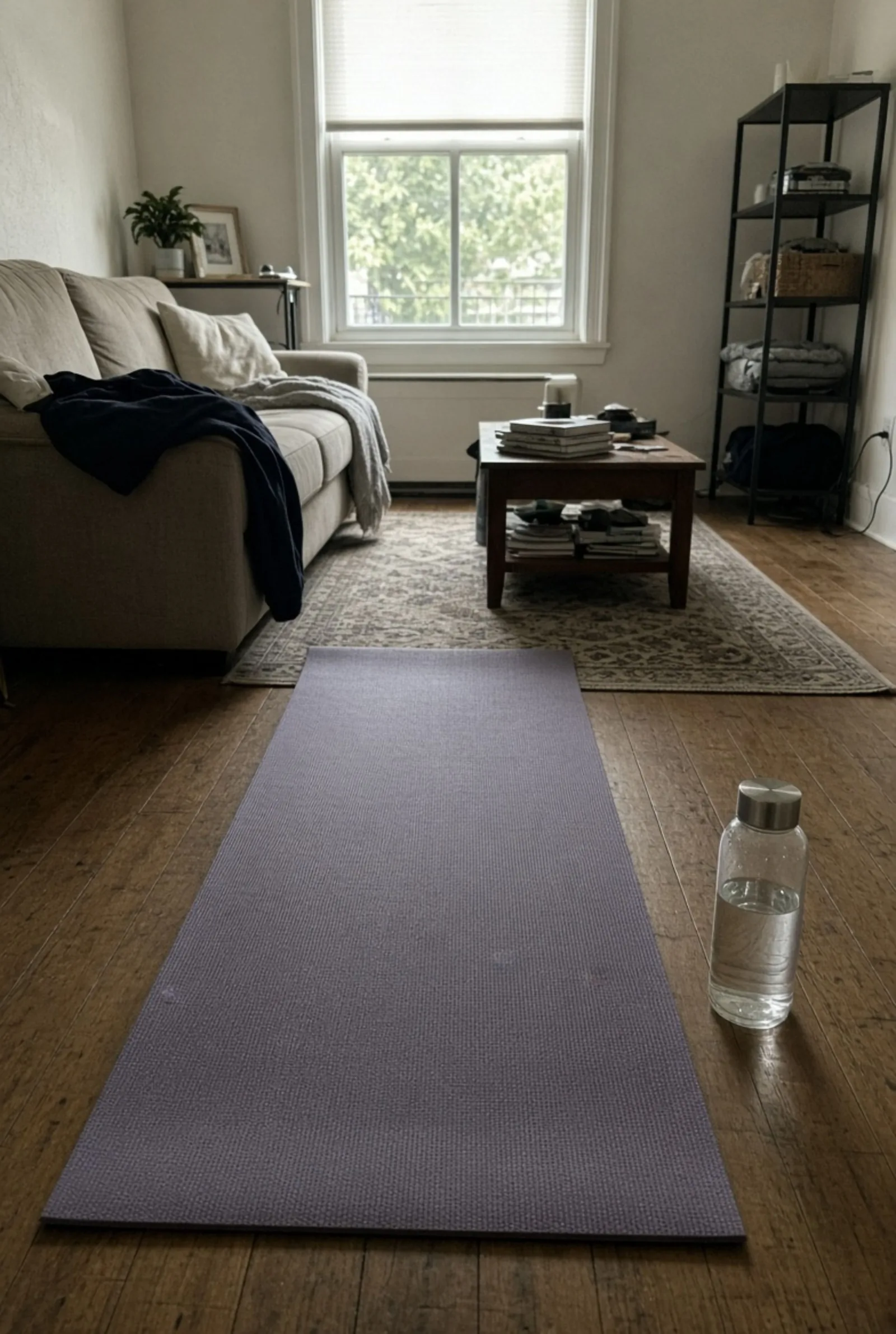 A rolled yoga mat and a reusable water bottle on a wooden floor in a living room