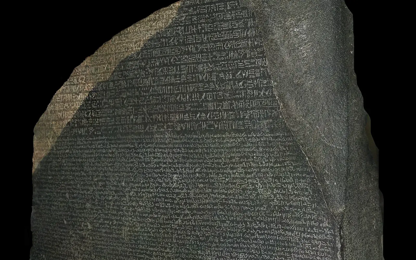 Close view of the dark grey Rosetta Stone, with rows of carved hieroglyphs at the top and dense lines of Demotic script below