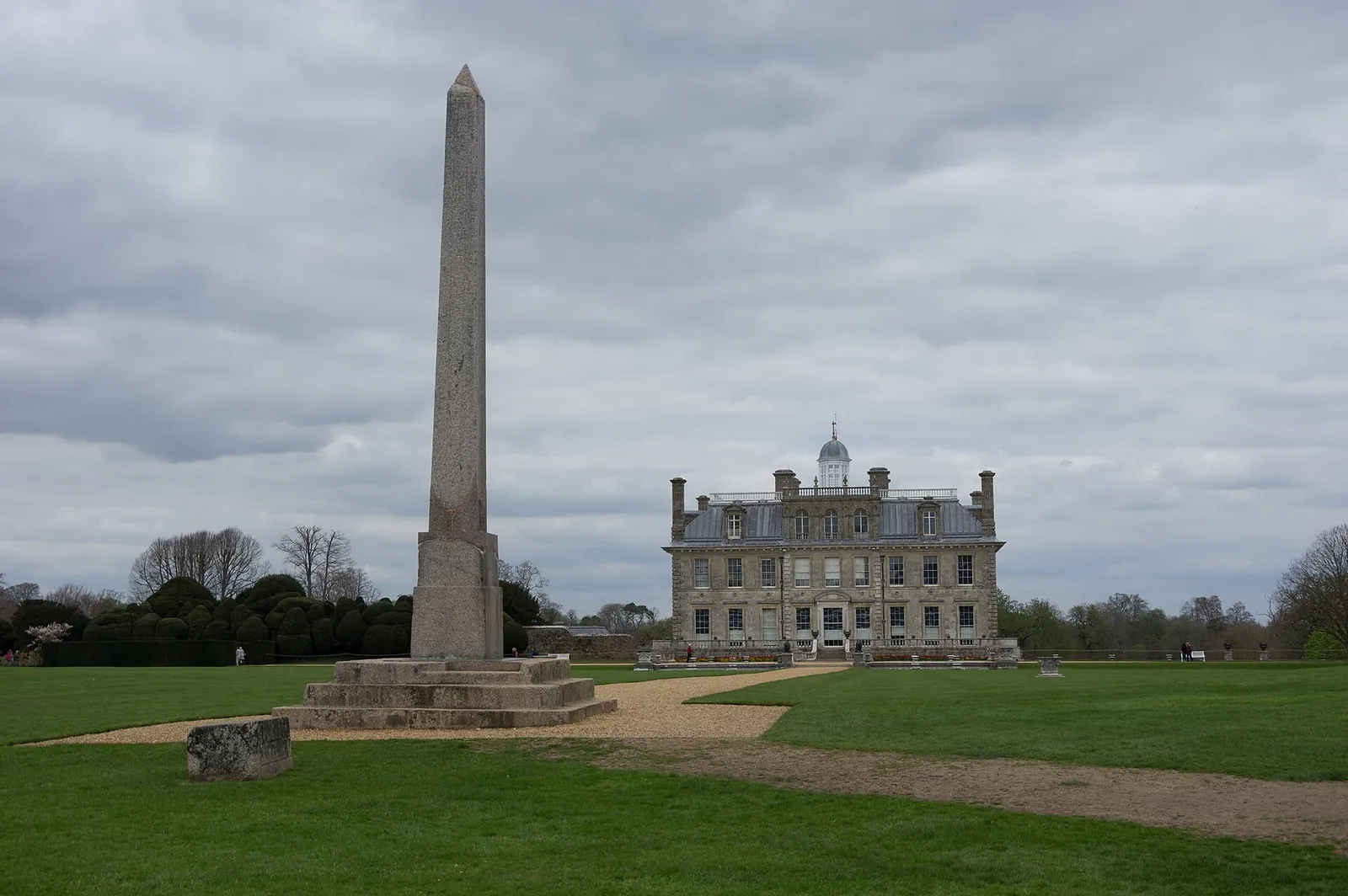A tall pink granite obelisk standing on a lawn in front of the pale stone Kingston Lacy country house in Dorset