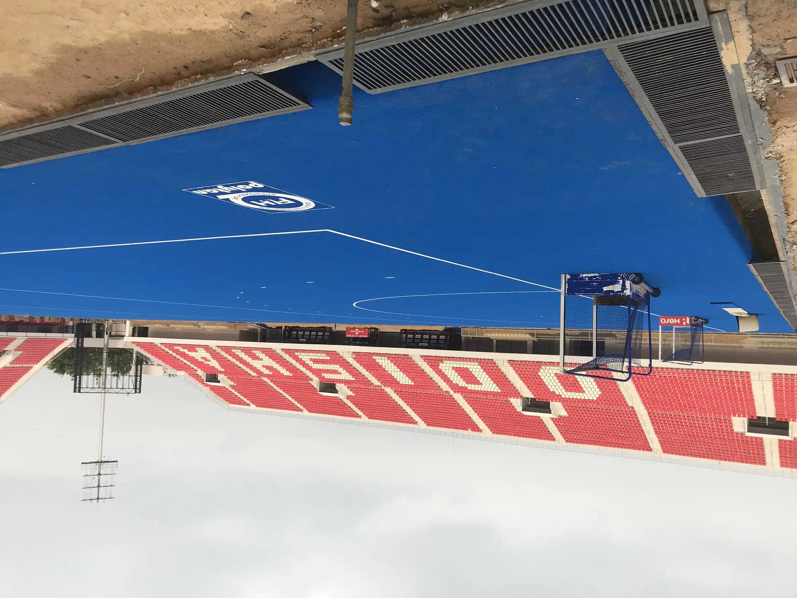 Wide view of the empty green turf and blue seating at Kalinga Hockey Stadium in Bhubaneswar, Odisha, under a cloudy sky