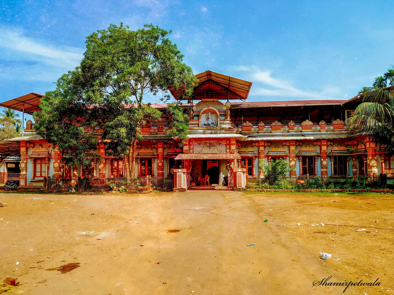 The ornate red and cream facade of the Edneer Mutt monastery building in Kasaragod, Kerala, under a blue sky