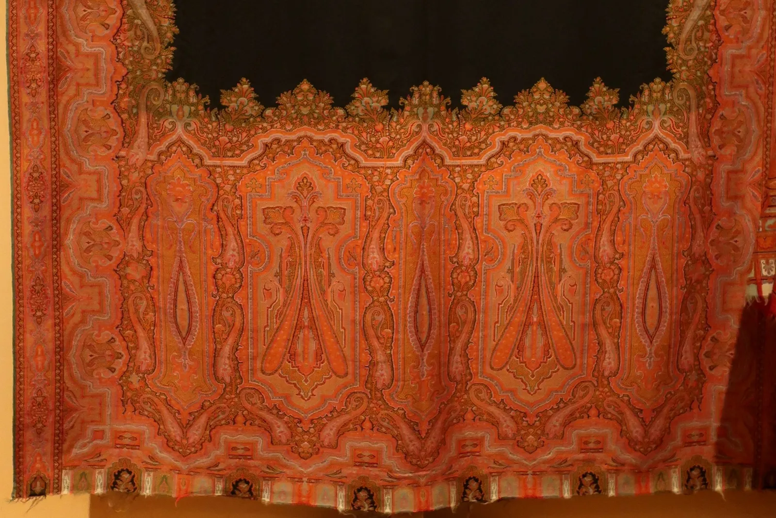 The lower border of a 19th-century Paisley shawl in orange, red and green, filled with tall curving teardrop motifs beneath a black centre panel