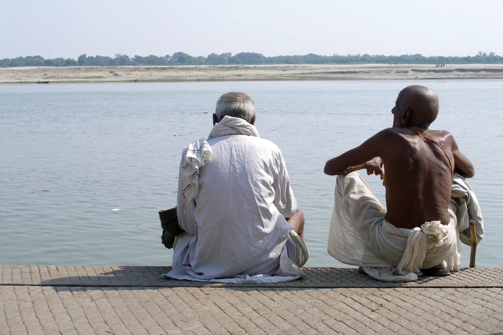Pilgrims sitting on stone steps beside the Ganges river at Varanasi under a hazy sky
