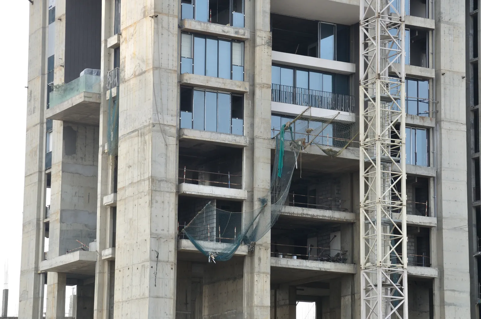 Concrete apartment tower under construction in Kolkata, with glass windows fitted on upper floors, safety netting and a tall white tower crane