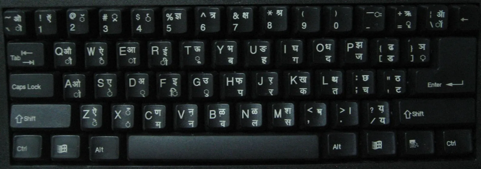 Close-up of a black computer keyboard with Hindi Devanagari letters printed beside the English letters on each key in the InScript layout