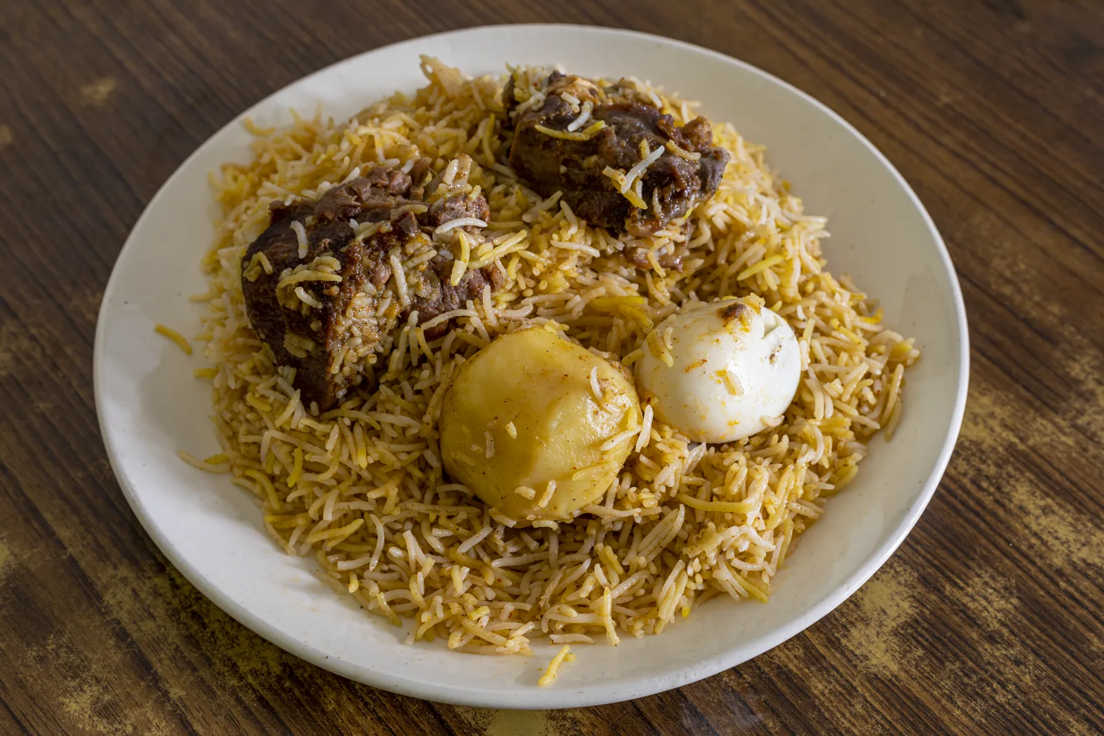 Kolkata-style mutton biryani on a plate with rice, meat and a large cooked potato piece