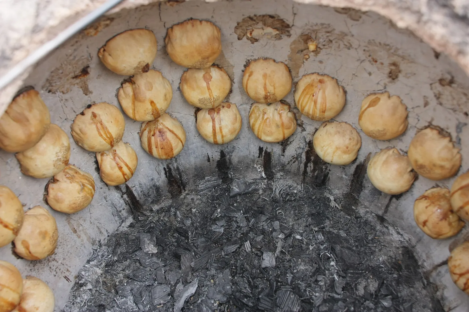 Round golden samsa pastries stuck to the inner wall of a clay tandoor oven above glowing charcoal in Khiva, Uzbekistan