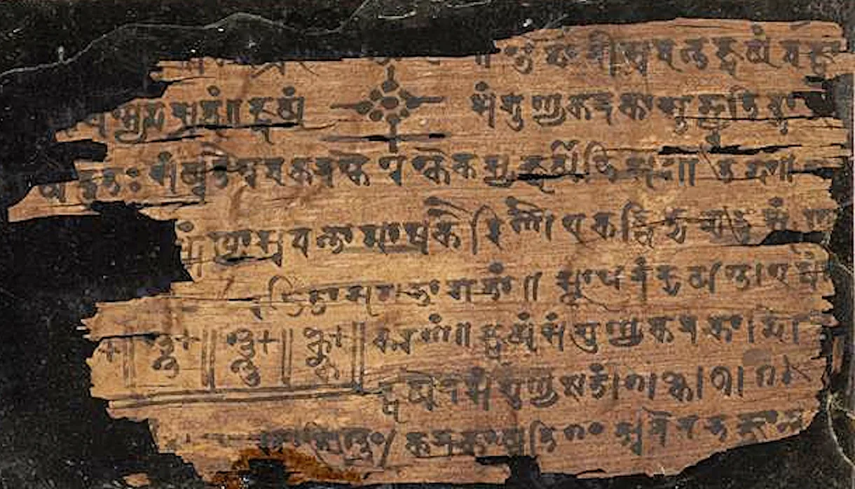 A fragile leaf of brown birch bark covered in rows of dark handwritten Sharada script, part of the Bakhshali manuscript