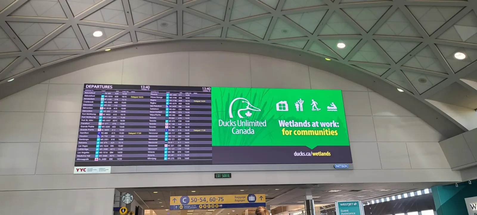 Large departures board under a curved white ceiling at Calgary International Airport, with the airport code YYC shown in the corner