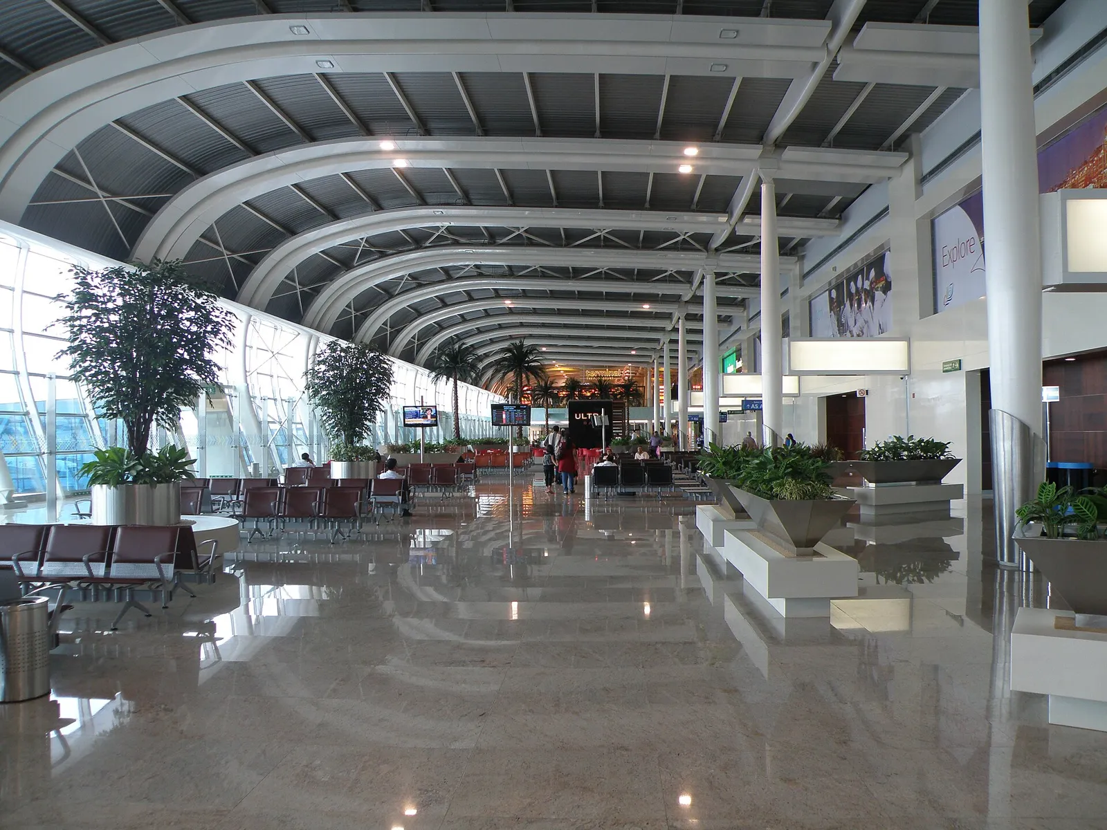Long, bright departure lounge at Mumbai airport's Terminal 1C, with arched white ceiling beams, potted plants and rows of seats