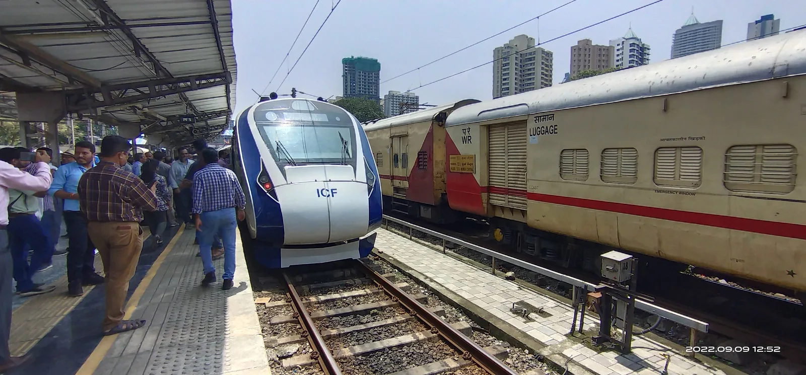 An orange and grey Vande Bharat Express trainset on broad-gauge track, photographed from the side with overhead wires above
