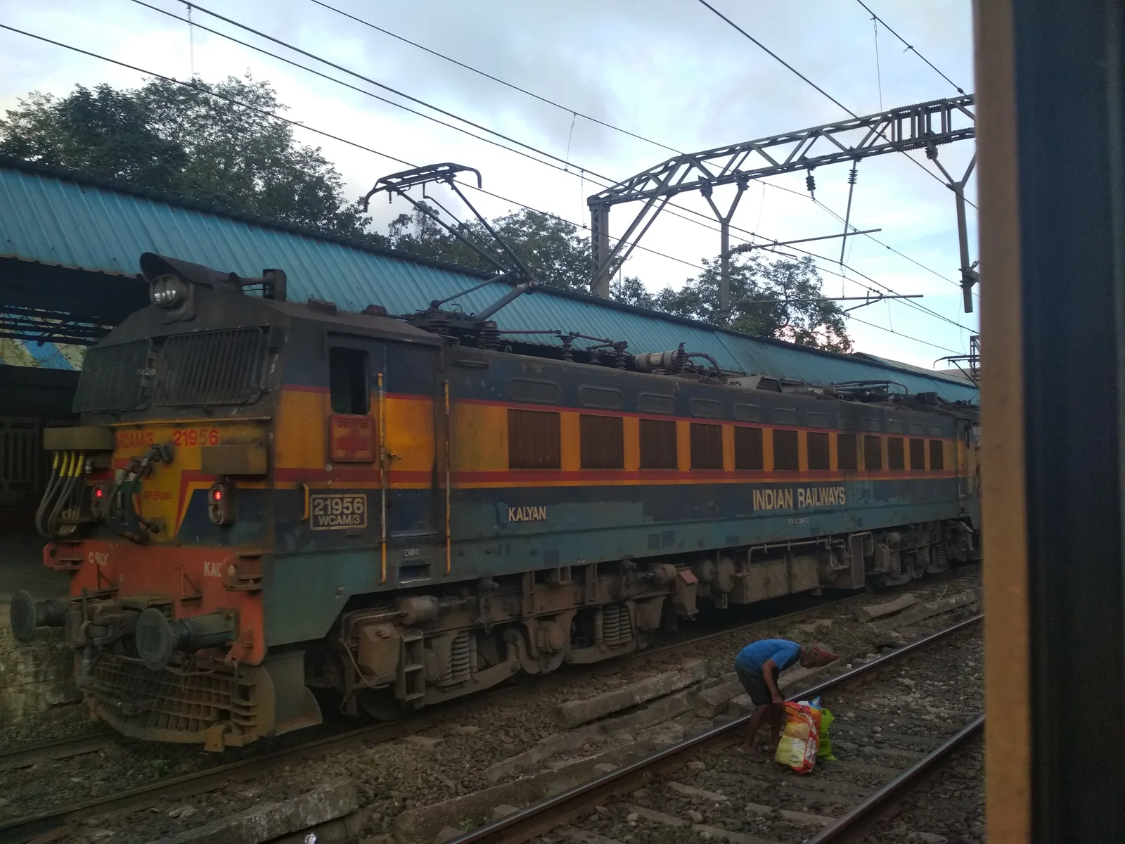 A blue and cream WCAM-3 electric locomotive hauling passenger coaches on the Mumbai to Pune line, with hills and overhead wires behind