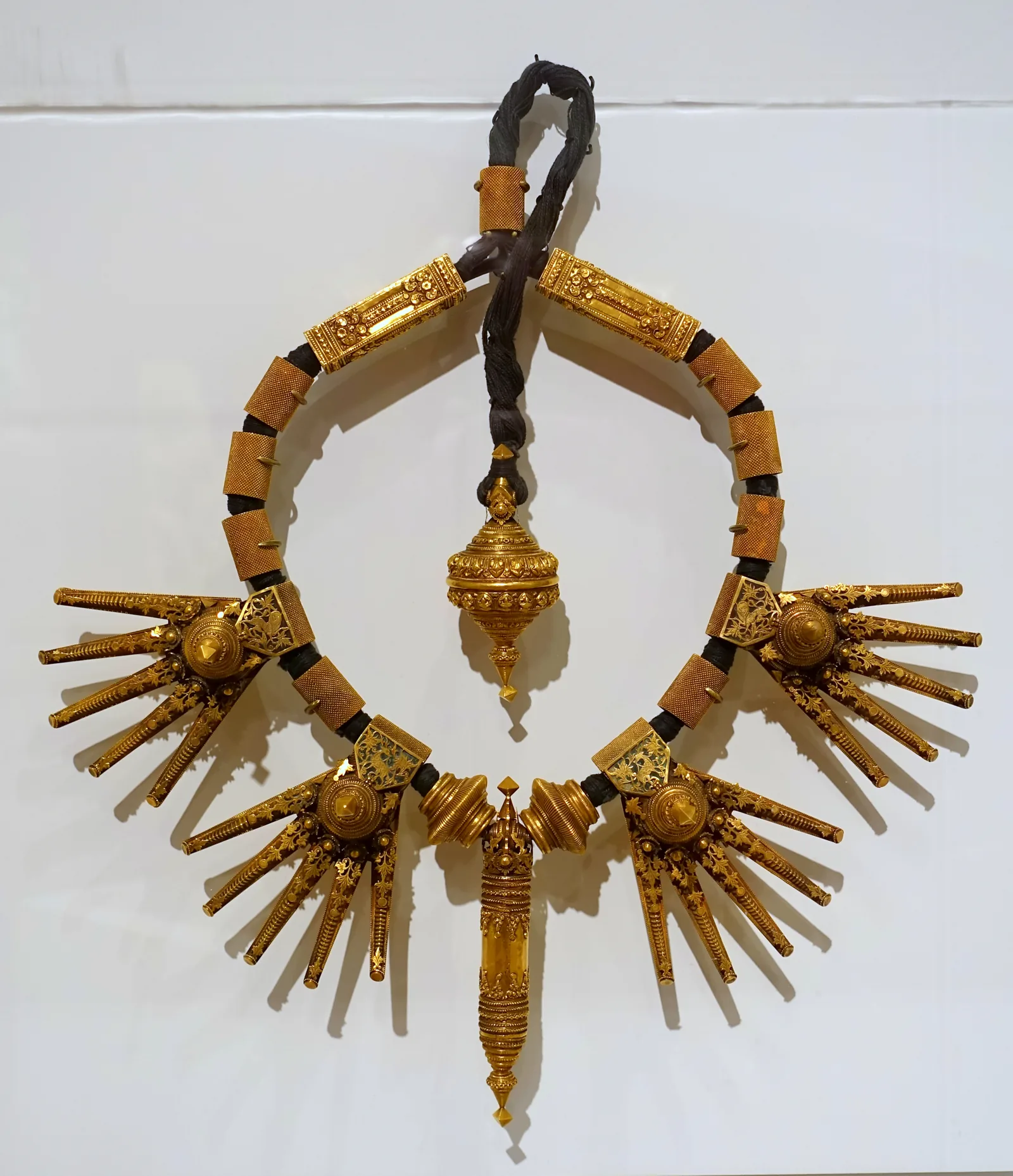 Ornate late-nineteenth-century Tamil Nadu marriage necklace of gold, with dense floral plaques and pendants, photographed in a museum case