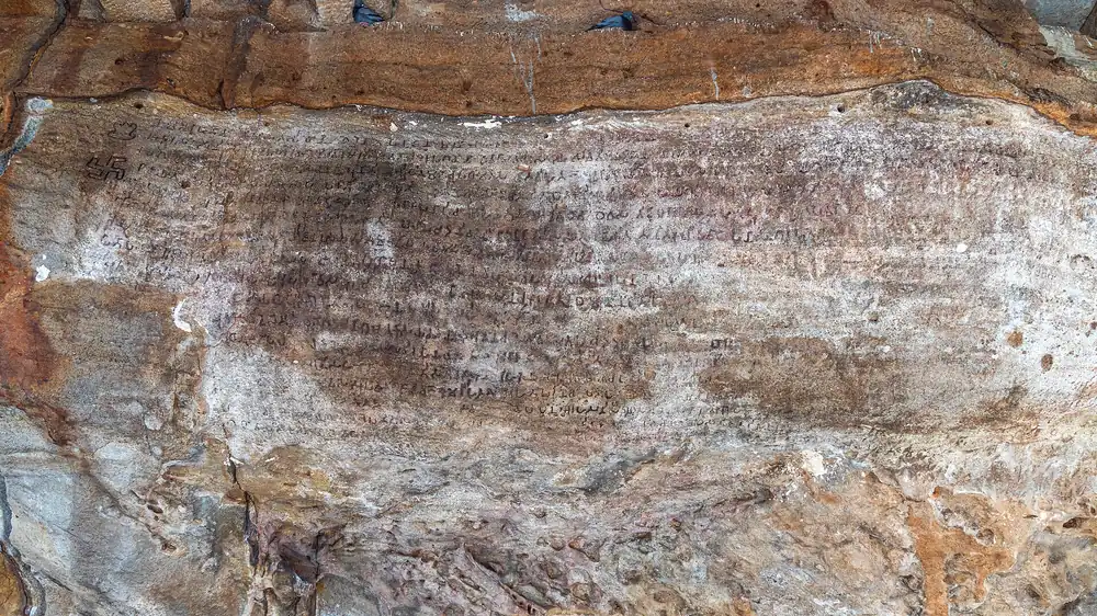 Lines of weathered Brahmi script carved across the rough orange and grey sandstone ceiling of the Hathigumpha cave in Odisha