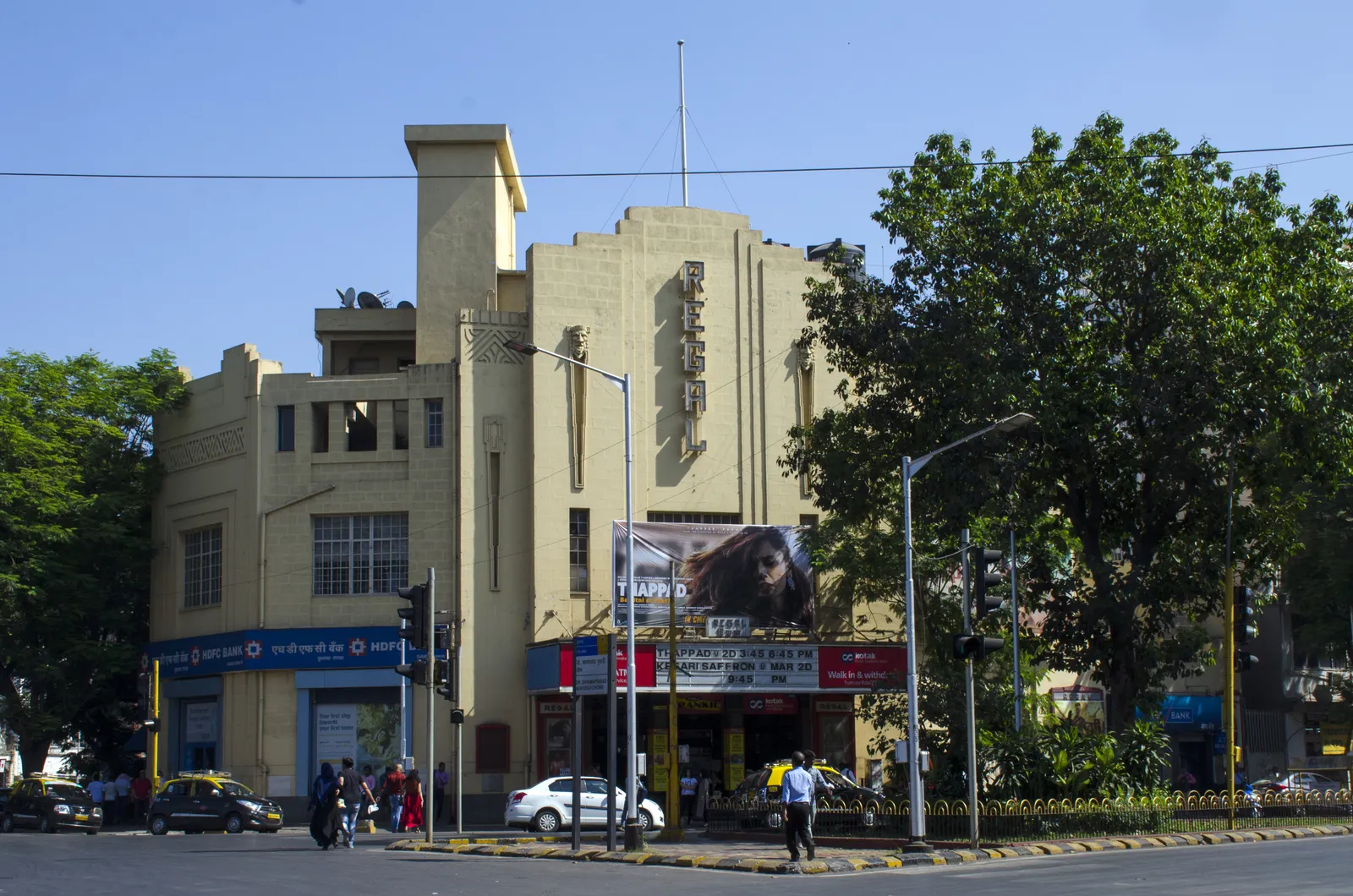 The cream Art Deco facade of Regal Cinema in south Mumbai, with a film poster above the entrance, street lamps and traffic in front