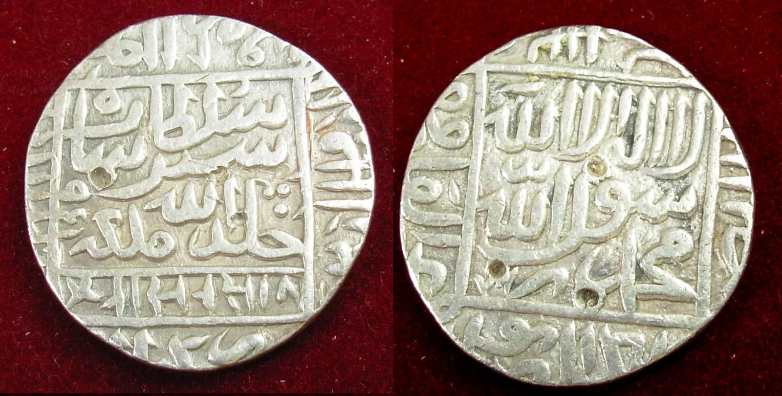 Both faces of a worn silver rupiya of Sher Shah Suri, with Persian and Arabic inscriptions in square panels, on red velvet