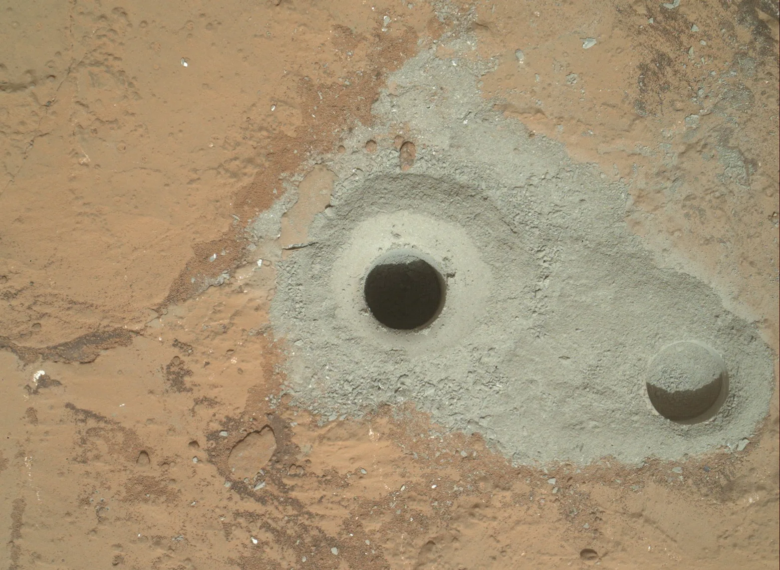 Close-up of a drill hole in reddish Martian rock, surrounded by a pile of pale grey powder that the drill brought up from below the surface
