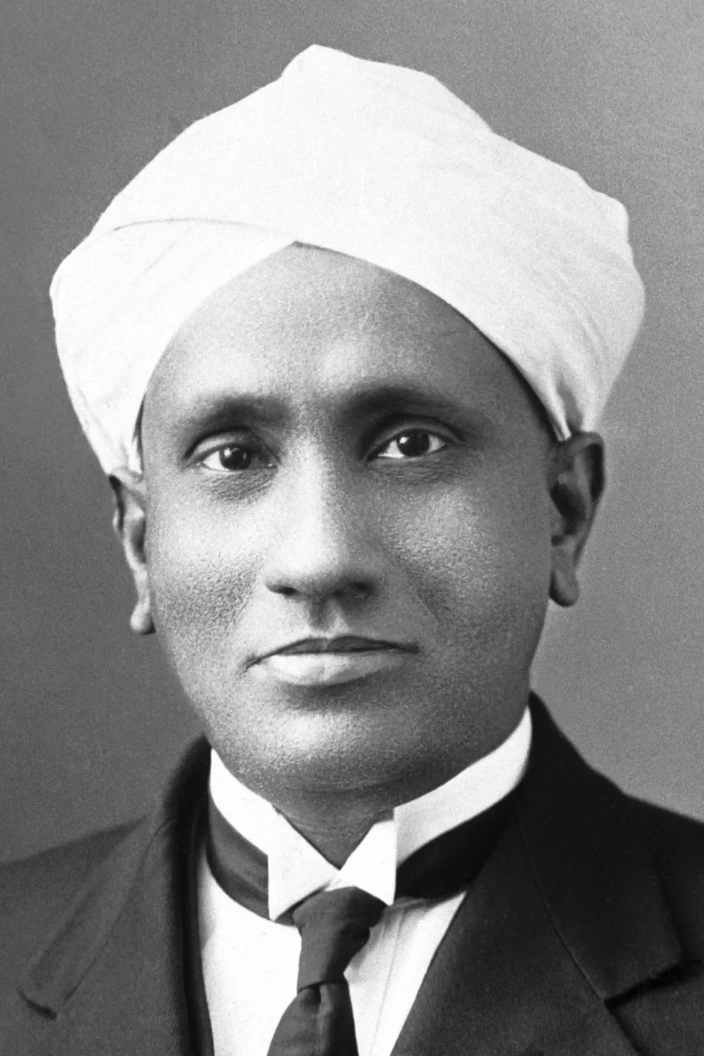 Black and white portrait of physicist C.V. Raman wearing a white turban, a dark suit and a tie