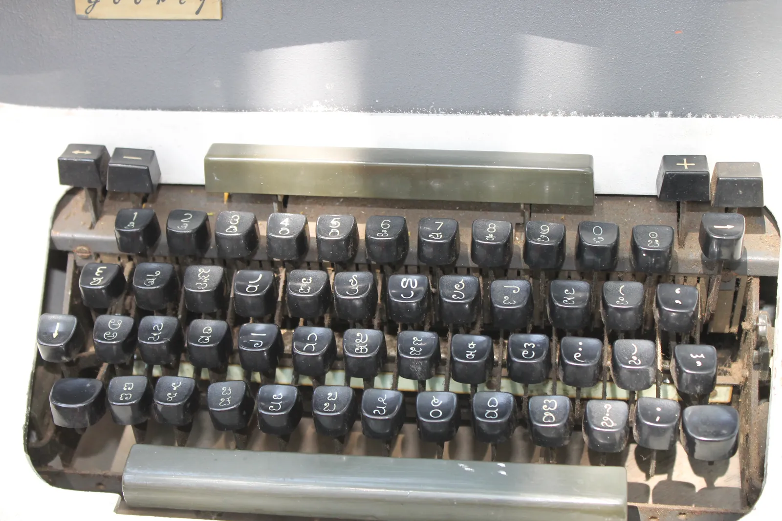 Close-up of a worn grey Godrej typewriter with black keys marked in Kannada script, used outside a government office
