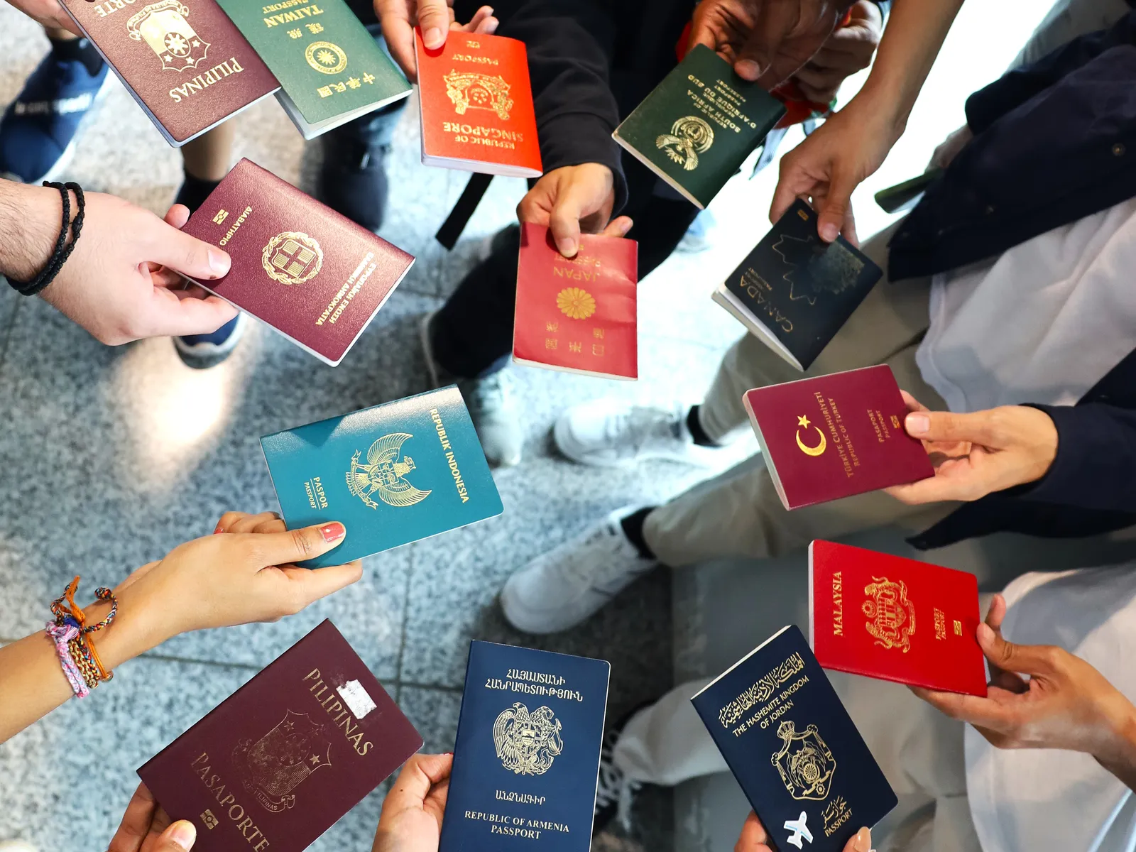 A circle of hands holding up passports from 11 countries, including burgundy Philippine and Turkish booklets, red Japanese, Singaporean and Malaysian ones, green Taiwanese and teal Indonesian covers, and dark blue Canadian, Armenian and Jordanian passports