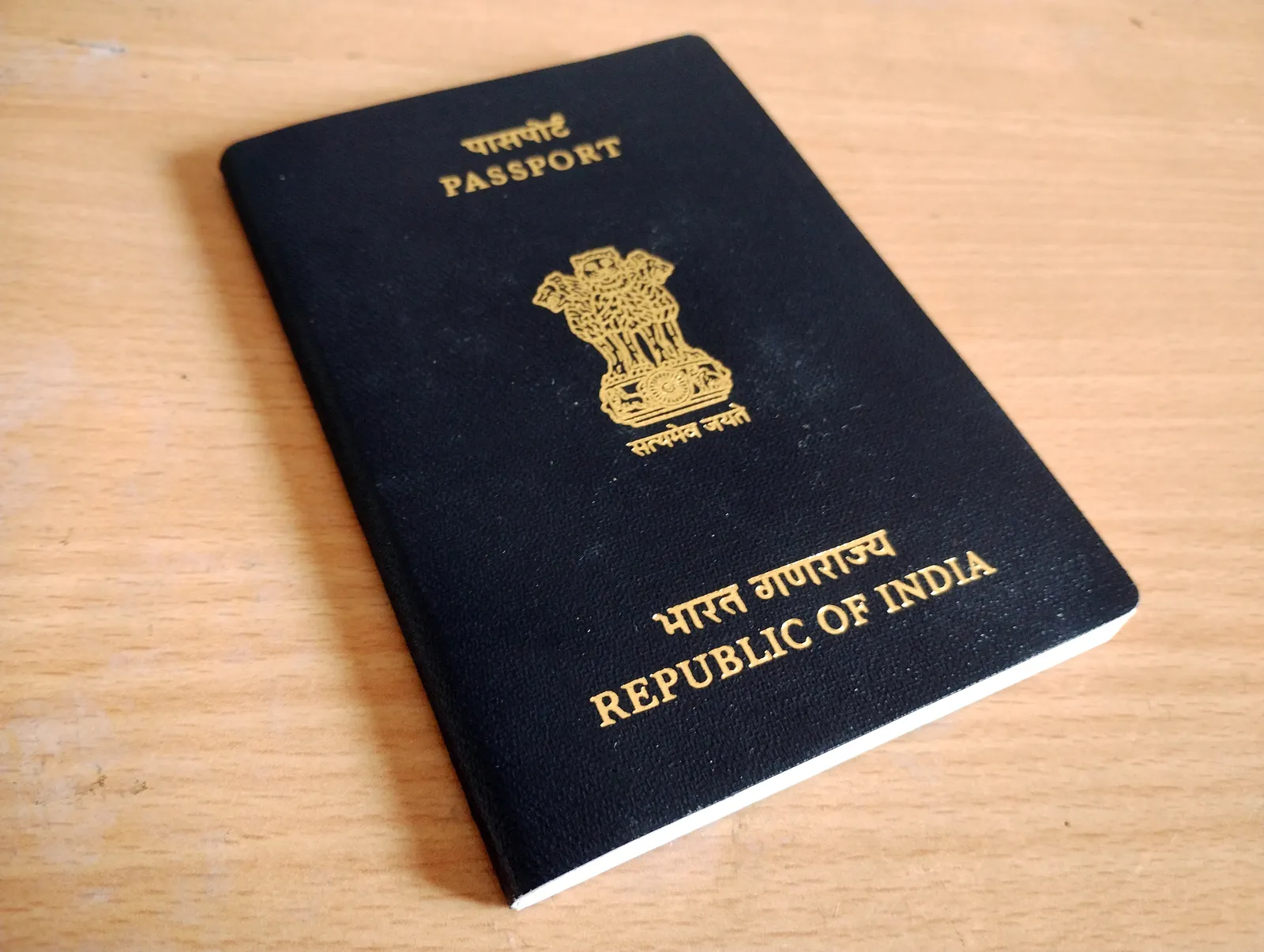 A navy blue Indian passport lying on a wooden table, with the national emblem and the words Passport and Republic of India stamped in gold in Hindi and English