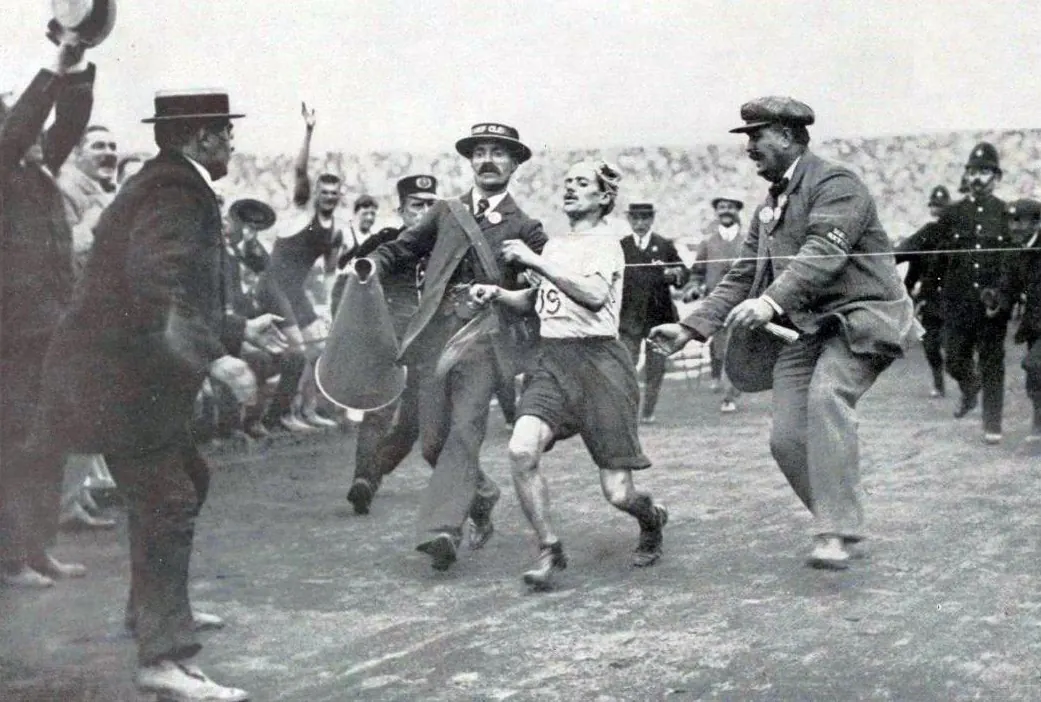 Black-and-white photo of officials helping an exhausted Dorando Pietri across the finish line in 1908