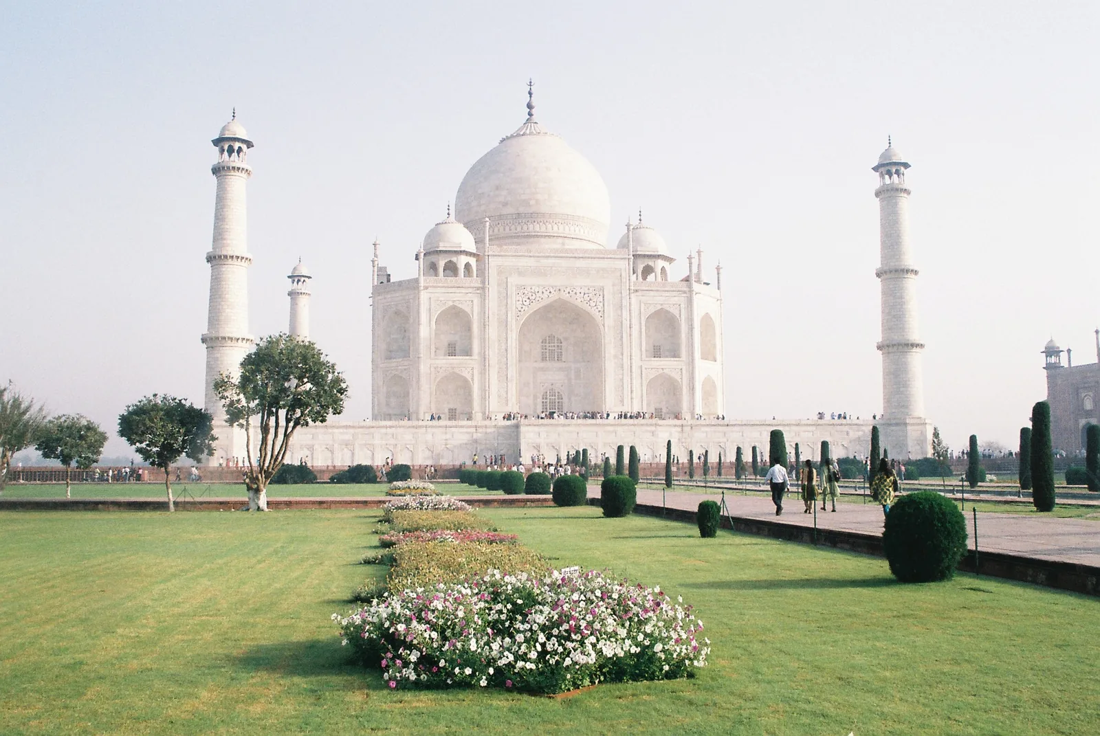View across the Taj Mahal charbagh garden with lawns, pathways and the white mausoleum beyond trees and a water channel